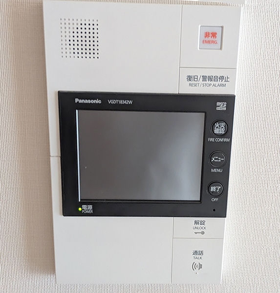 : 光センサーが取り付けられていない、Panasonic製（型番VGD18342W）のオートロック対応集合住宅用インターホン（親機）。 （黒い液晶画面と、非常、復旧/警報音停止、メニュー、終了、解錠、通話などのボタンが配置された一般的なインターホンの写真。）