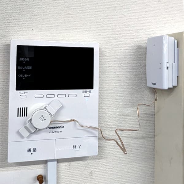 パナソニック製テレビドアホン VL-MWE310に音・振動センサーを設置した例。インターホンのスピーカー部分に円形センサーを取り付け、壁に固定されたREVEX製センサー本体に接続。