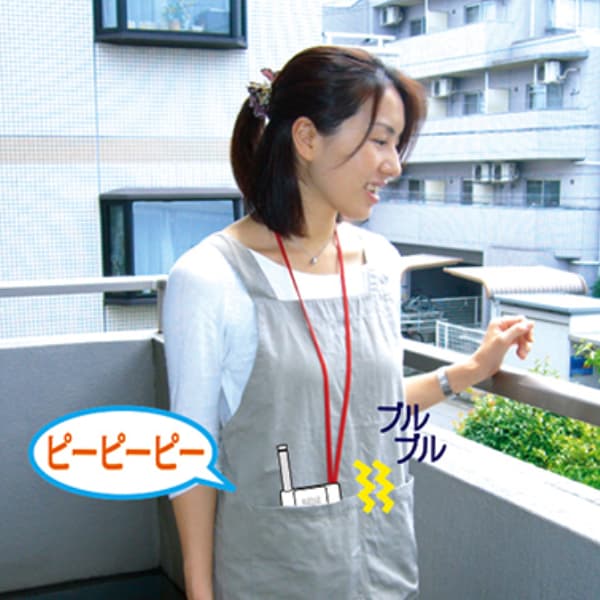 バルコニーに立つエプロン姿の女性。首から下げた白い小型装置が作動し、「ピーピーピー」という音と「ブルブル」という振動を表す文字と記号が添えられている。
